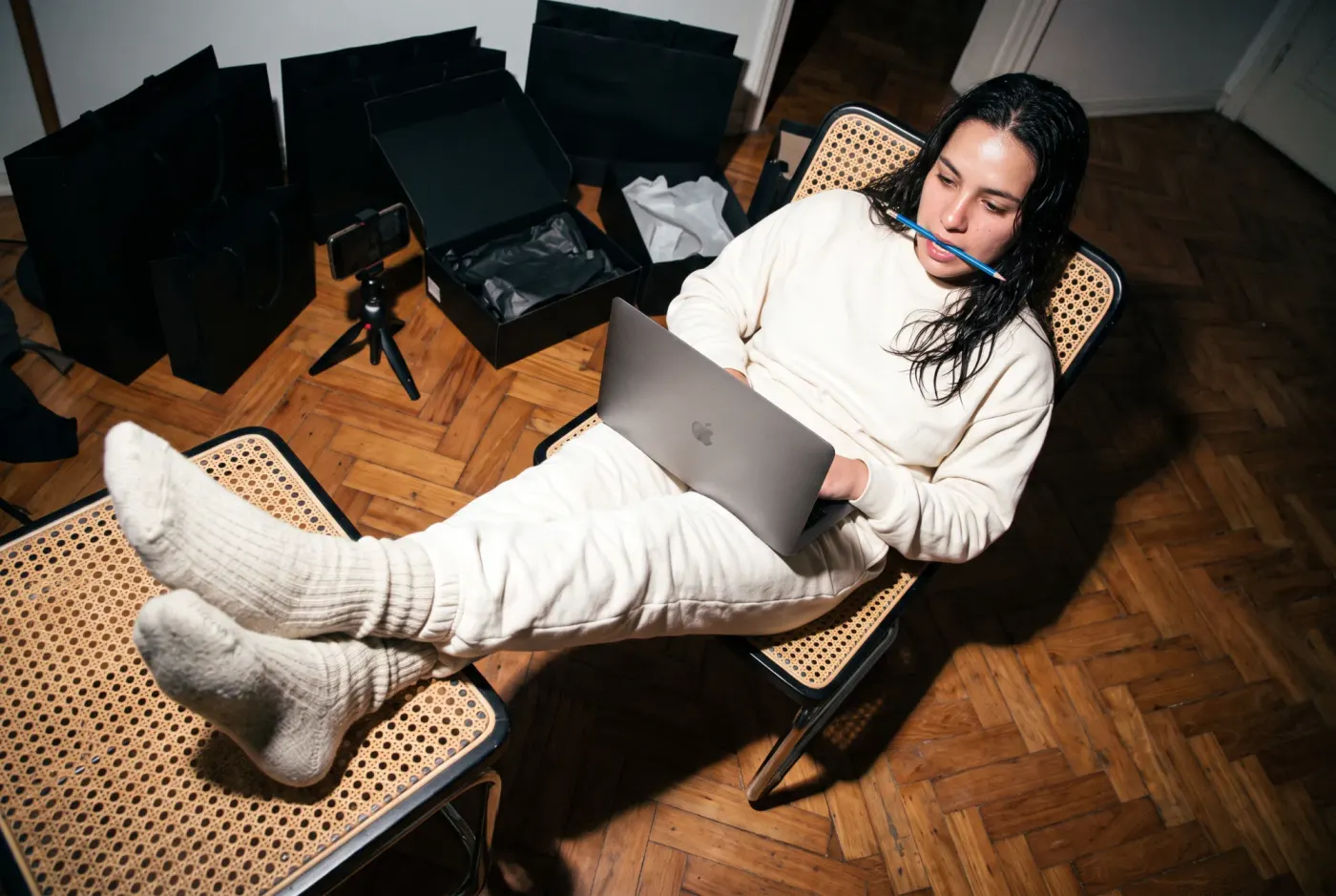 Creator com o notebook no colo revisando números, cercada de caixas e sacolas