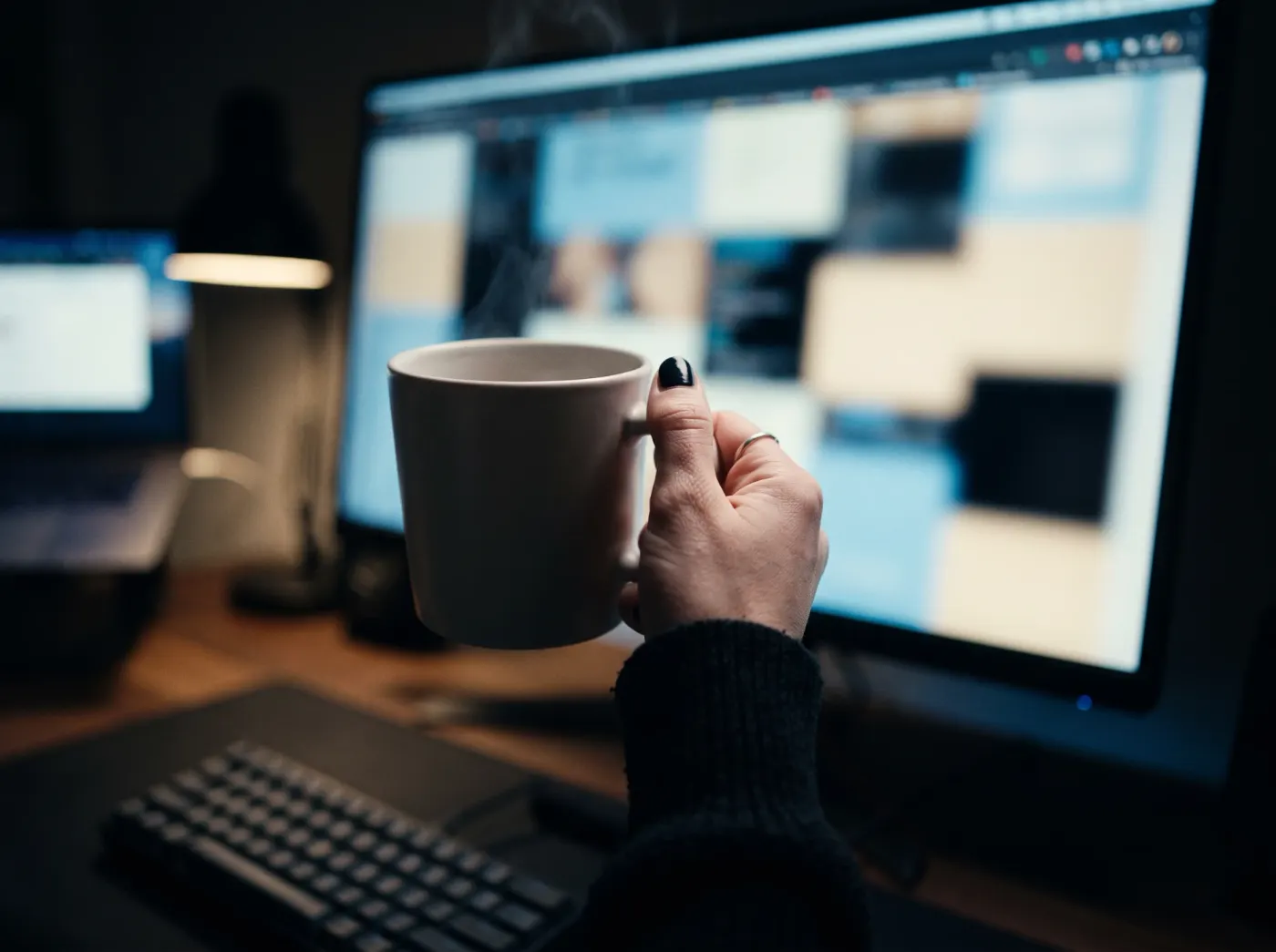 Mão com uma caneca diante de um monitor exibindo painel de conteúdos e métricas
